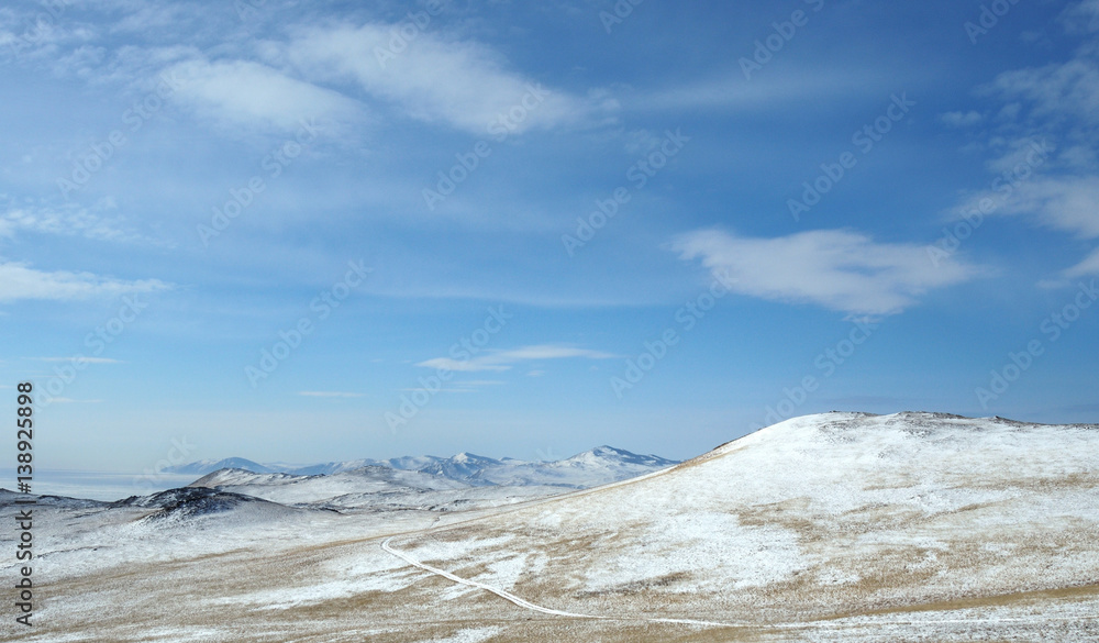 Mountain winter landscape. with high hills Olkhon offers beautiful views of Lake Baikal, covered with ice. Snow-capped mountains on the horizon. Sunny day. Photo partially tinted.