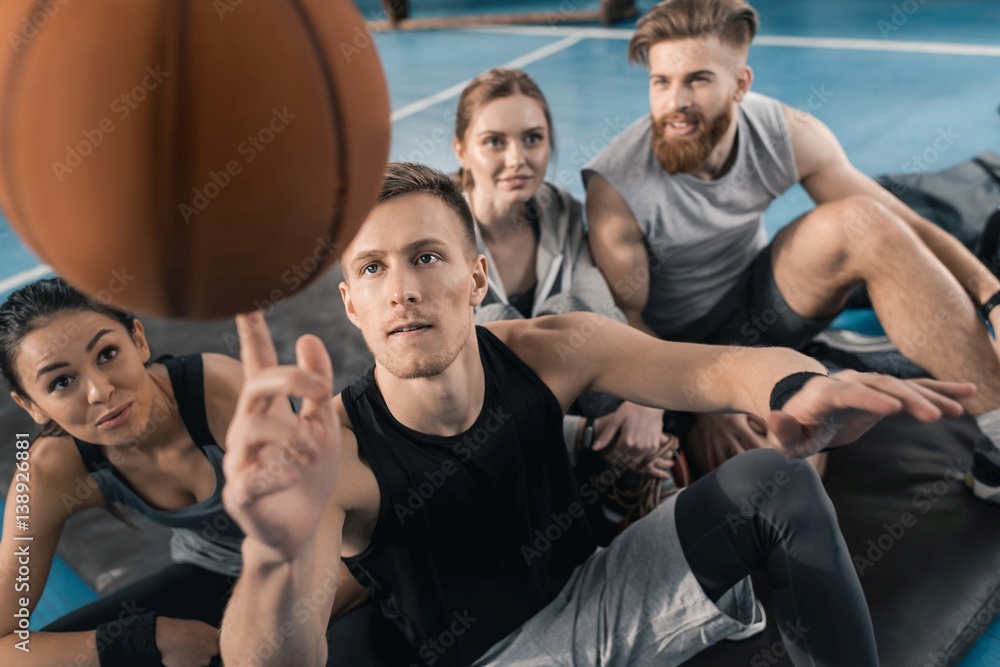 Sporty young people looking at man balancing ball on finger Sporty young people looking at man balancing ball on finger