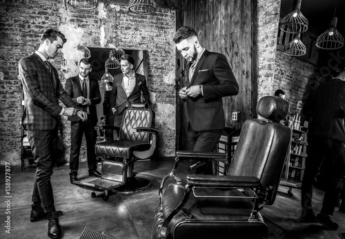 Group of young elegant positive mens pose in interior of barbershop. Black-white photo.