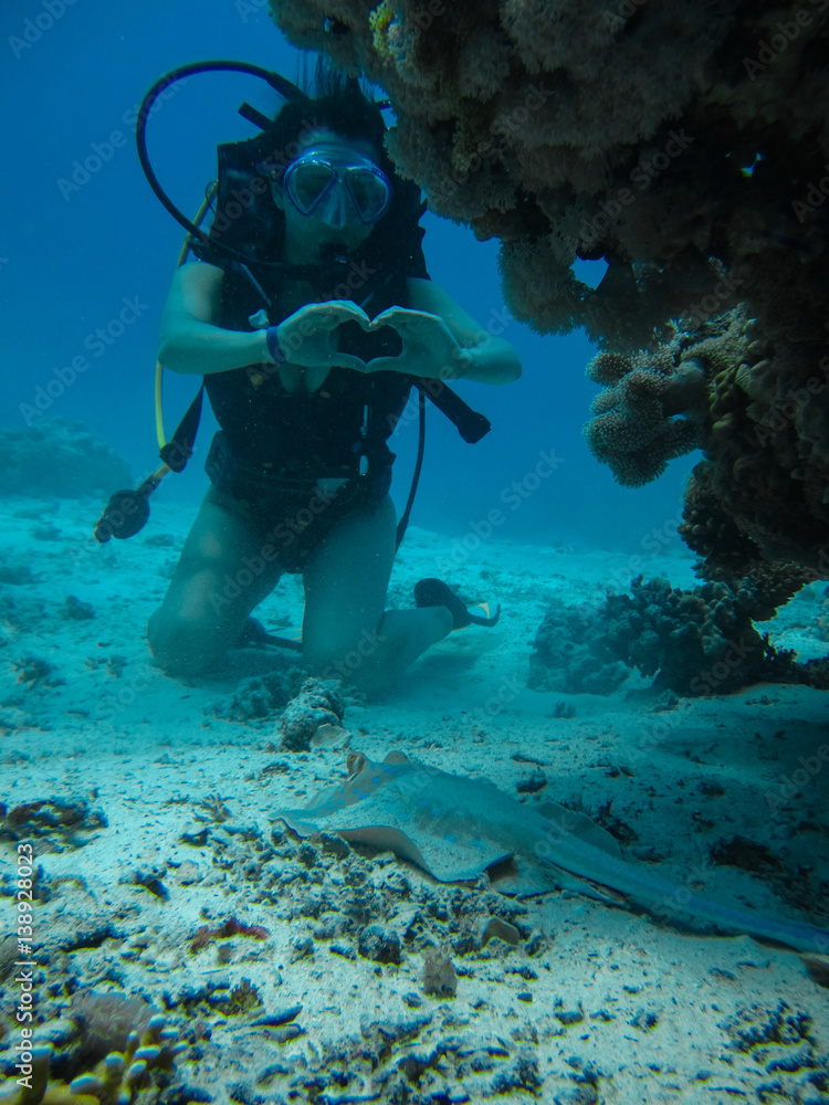 Young woman on the seafloor showing love signal to a small slope while diving Young woman on the seafloor showing love signal to a small slope while diving