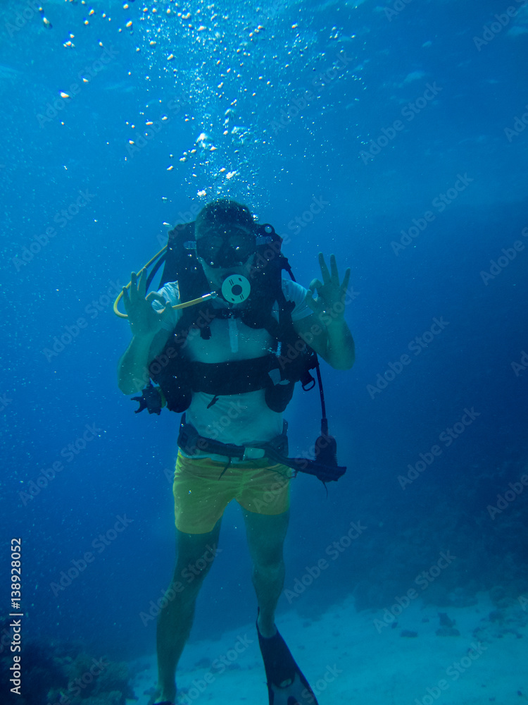 Underwater shoot of a man diving looking at the camera and showing ok Underwater shoot of a man diving looking at the camera and showing ok