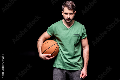 portrait of serious man with basketball ball looking to camera on black