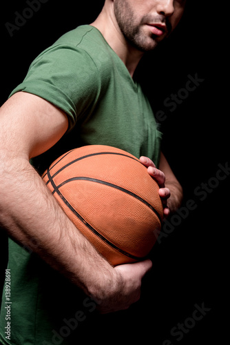 partial side view of man holding basketball ball in hands on black