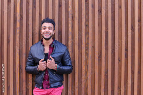 Nice-Looking Arabian Young Man Stands Near Wall and Smiles, Laug photo