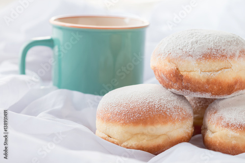 Jelly filled doughnuts and a coffee mug in white sheets on a bed