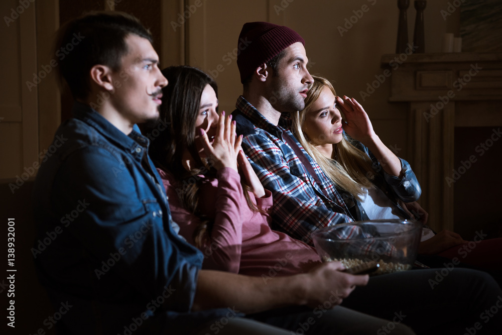 side view of scared friends watching movie with popcorn at home side view of scared friends watching movie with popcorn at home