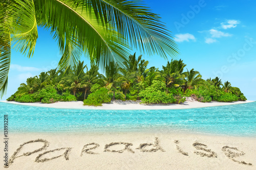 Whole tropical island within atoll in tropical Ocean and inscription "Paradise" in the sand on a tropical island.