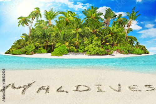 Whole tropical island within atoll in tropical Ocean and inscription "Maldives" in the sand on a tropical island, Maldives.