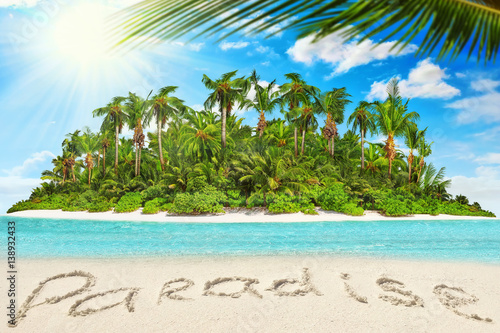 Whole tropical island within atoll in tropical Ocean and inscription "Paradise" in the sand on a tropical island.