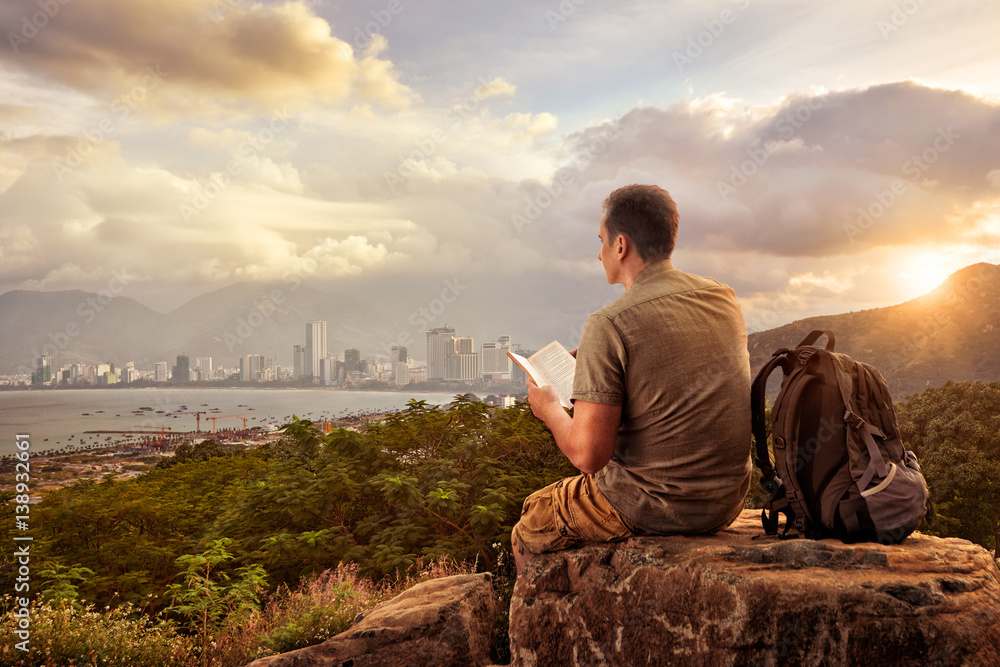 hiker with backpack sitting on top of mountain enjoying view coast a modern city