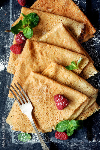 Crepes with raspberries - Food & Drink
Delicious homemade whole wheat crepes served with fresh raspberries, mint leaf and sugar powder on slate. Top view, closeup, vertical image