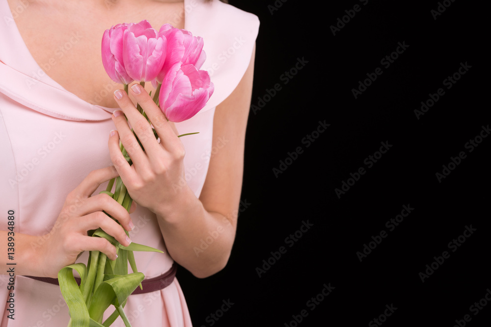 Close-up partial view of woman in dress holding pink tulips on black, international womens day concept Close-up partial view of woman in dress holding pink tulips on black, international womens day concept