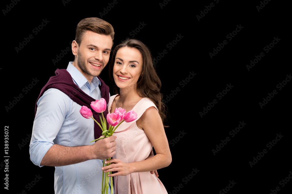 portrait of smiling couple in love holding tulips bouquet and looking to camera on black, international womens day concept portrait of smiling couple in love holding tulips bouquet and looking to camera on black, international womens day concept