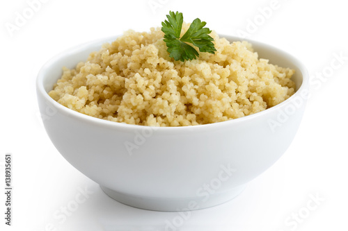 Cooked couscous with green parsley in white ceramic bowl isolated on white.