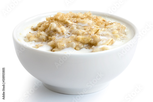 Cooked whole porridge oats with milk and brown sugar in white ceramic bowl isolated on white.