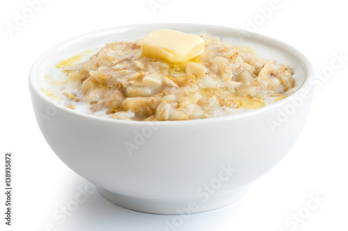 Cooked whole porridge oats with milk and butter in white ceramic bowl isolated on white.