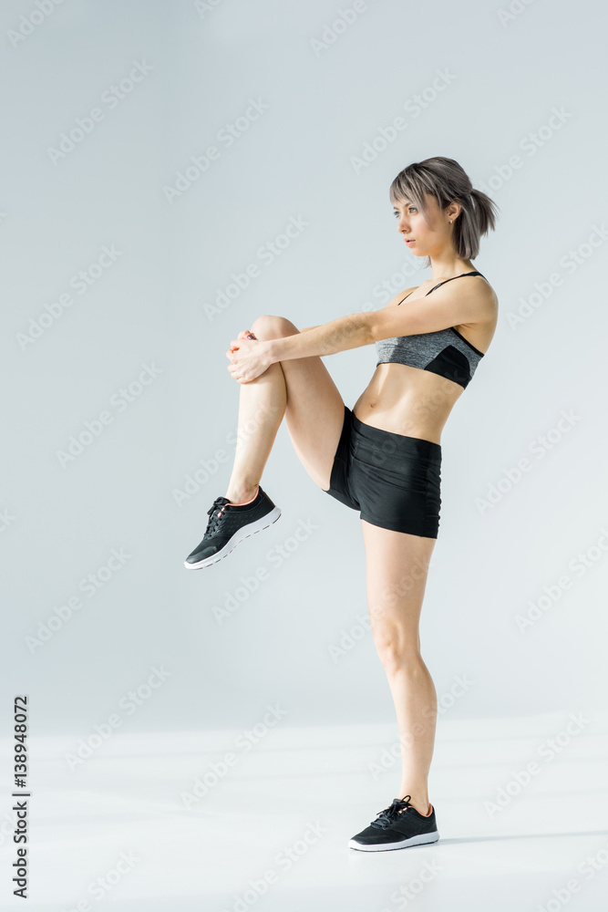 Side view of young athletic woman in sportswear exercising and looking away on grey Side view of young athletic woman in sportswear exercising and looking away on grey