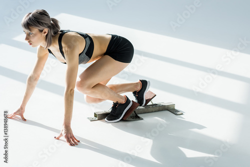 side view of sporty woman in starting position on grey