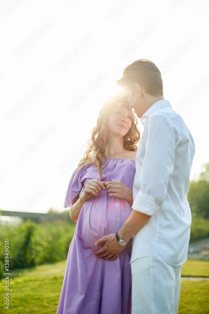 Pregnant woman and her husband walks in park at evening. Family enjoying pregnancy. The concept of Mother's Day and Women's Day.