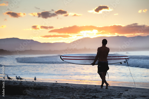 Tableau sur toile Surfer walking on the shore along the beach lokking at the stunning sunset in Byron Bay, NSW, Australia