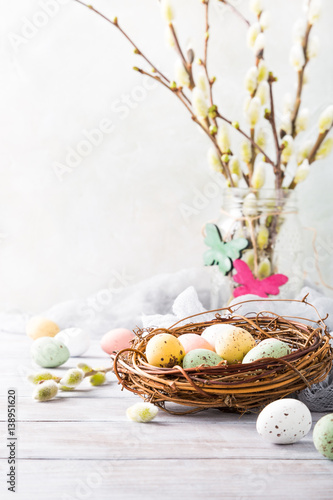 Easter composition of colorful quail eggs in the nest on the light wooden background. Holiday concept with copy space.