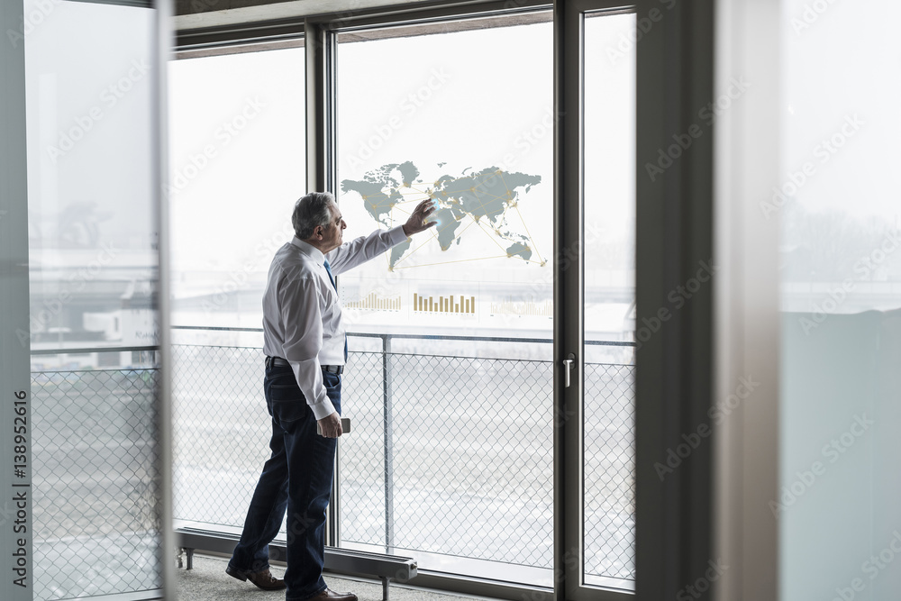 Businessman touching windowpane with world map in office Businessman touching windowpane with world map in office
