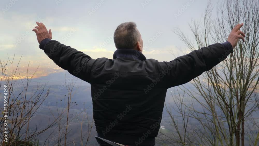 Man on hill raises his arms to the sky- back view Man on hill raises his arms to the sky- back view