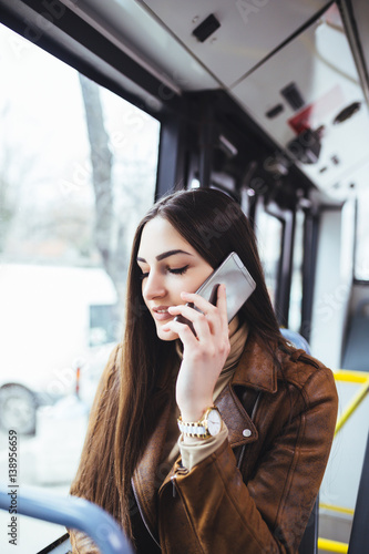 Beautiful young woman sitting in city bus and talking on mobile phone. 