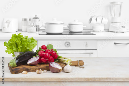 Wooden table with vegetables on top over blurred kitchen interior