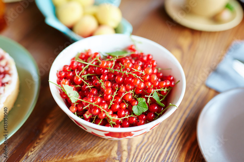 Close-up view of freshly collected ripe redcurrant lying in plate on wooden table