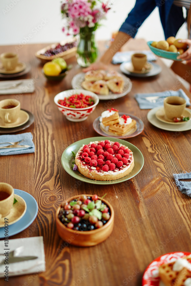 Wooden table covered with delicious freshly baked raspberry tart, homemade waffles, bowls with garden berries and cups of tea Wooden table covered with delicious freshly baked raspberry tart, homemade waffles, bowls with garden berries and cups of tea
