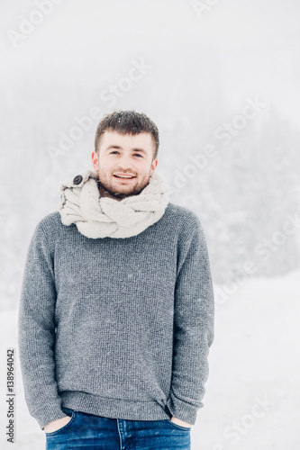 Man holds his hands in the pockets posing under falling snow photo