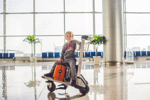 Cute little boy with orange suitcase at airport. The boy on the trolley and the airport photo