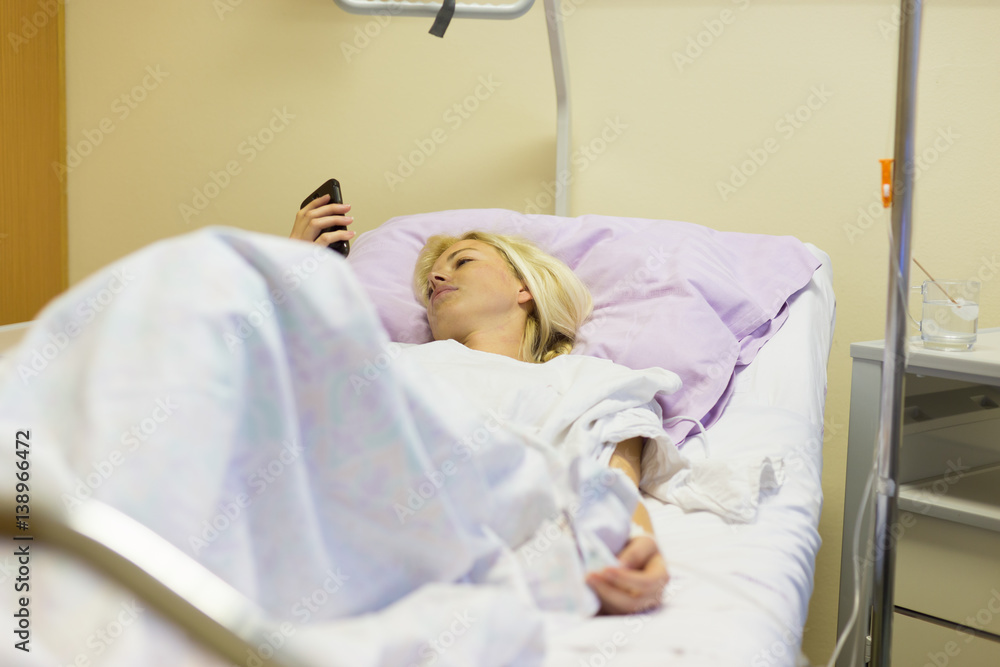 Bedridden female patient lying in hospital bed, using mobile phone