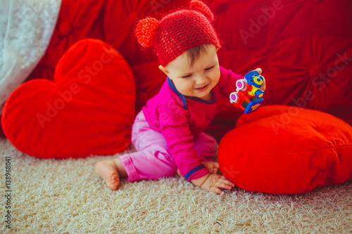 Funny child in red hat sits before red bed photo