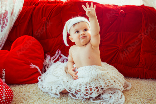 White scarf enveloped little child sitting before luxury red bed photo