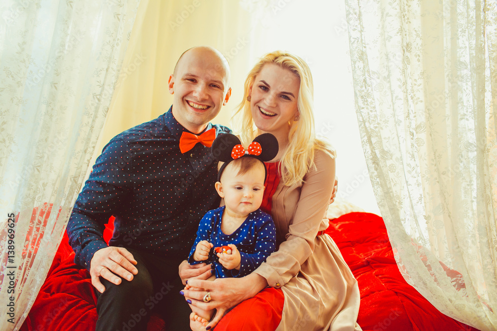 Φωτογραφία Happy mother and father hold their little daughter in Minnie Mouse ears sitting
