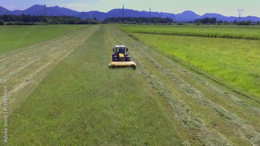 A yellow tractor is driving across a large meadow and is cutting grass. It is a nice summer day.
A yellow tractor is driving across a large meadow and is cutting grass. It is a nice summer day.