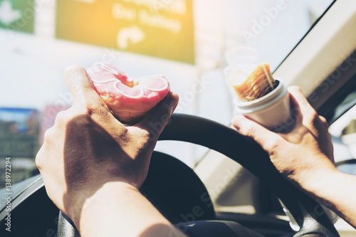 Man eating donuts and potato chip while driving car - multitasking unsafe driving concept
