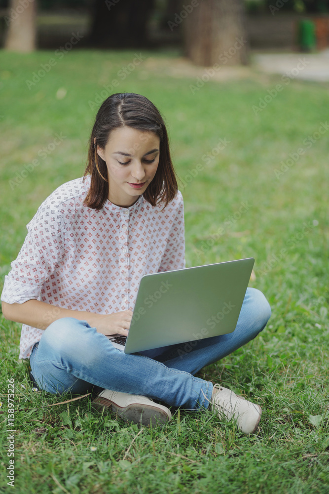 Young woman with laptop sitting on green grass Young woman with laptop sitting on green grass