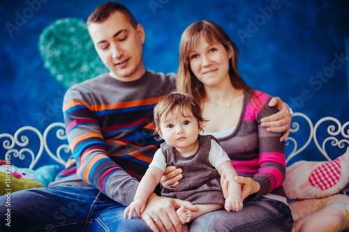 Happy parents hold little girl in grey dress on their knees