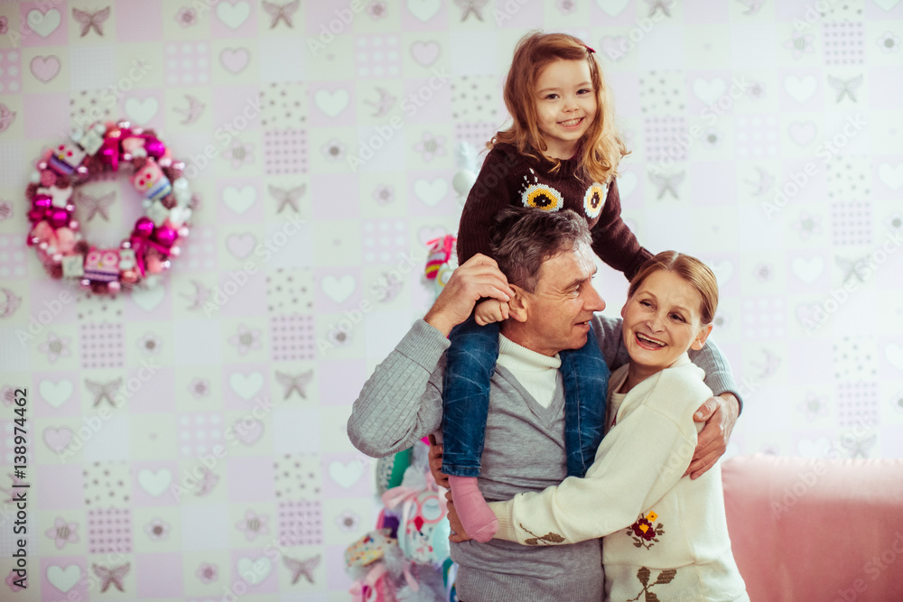 Old couple holds little girl on their neck posing in cosy room