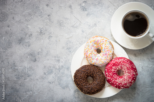 Colorful donuts and cup of coffee at concrete table. Top view copy space