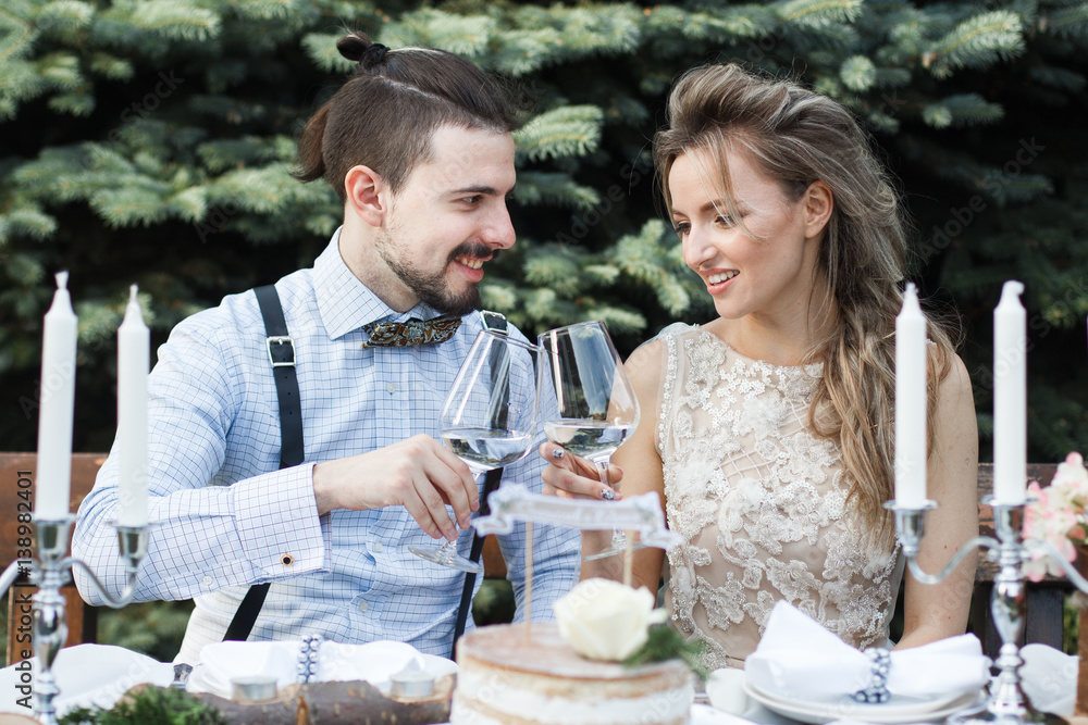 Groom and bride drinking champagne on a table in a decorative autumn forest, happy newlyweds Groom and bride drinking champagne on a table in a decorative autumn forest, happy newlyweds