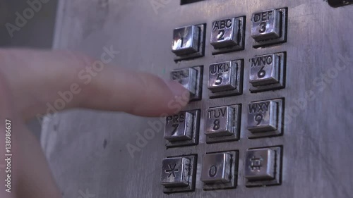 Person dialing number at payphone in public area.