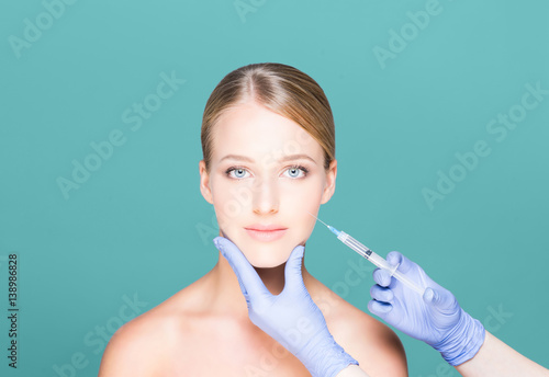 Young and beautiful woman having skin injections over teal background. Plastic surgery concept.