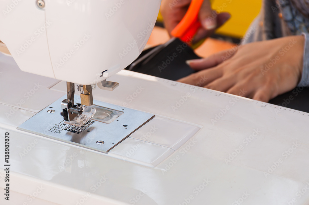 Sewing machine focusing at its presser foot with blurred woman's hands cutting cloth