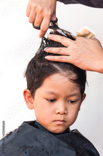 A boy is cut his hair by hair dresser over white background, focus at his right eyes