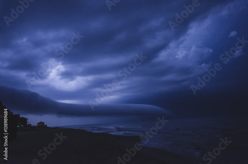 Thunderstorm over the sea, dark blue three-dimensional clouds illuminated by lightning flashes