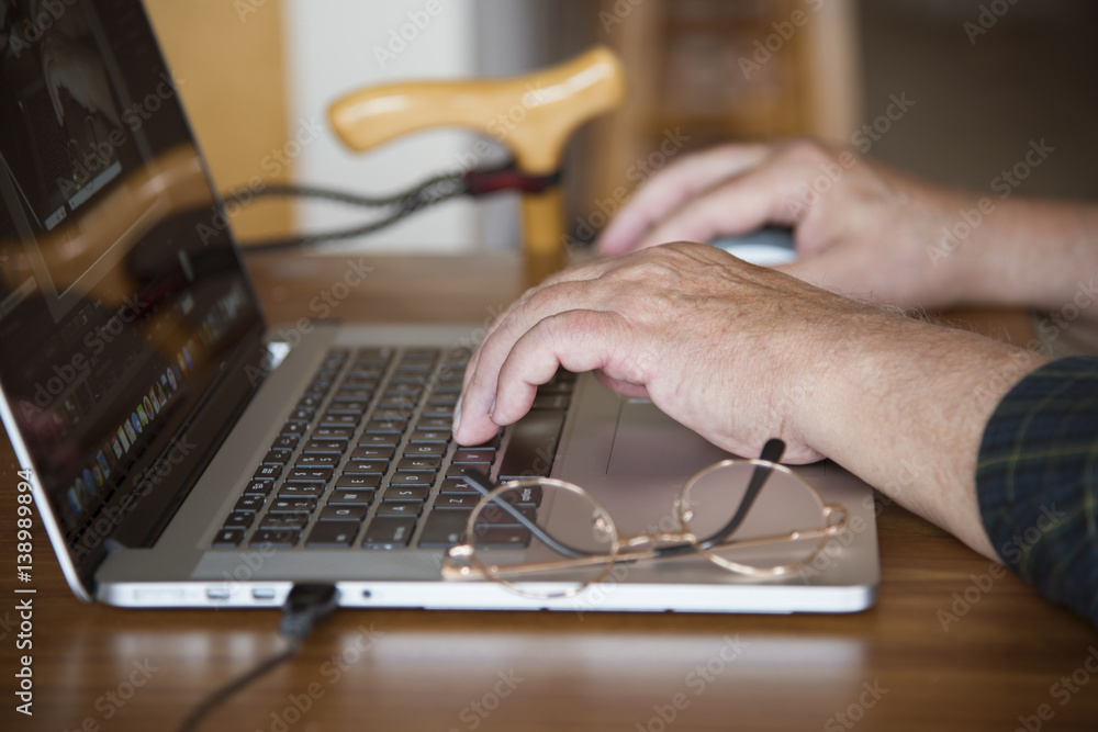 Old man's hands on computer keyboard with reading glasses and cane, shallow depth of focus